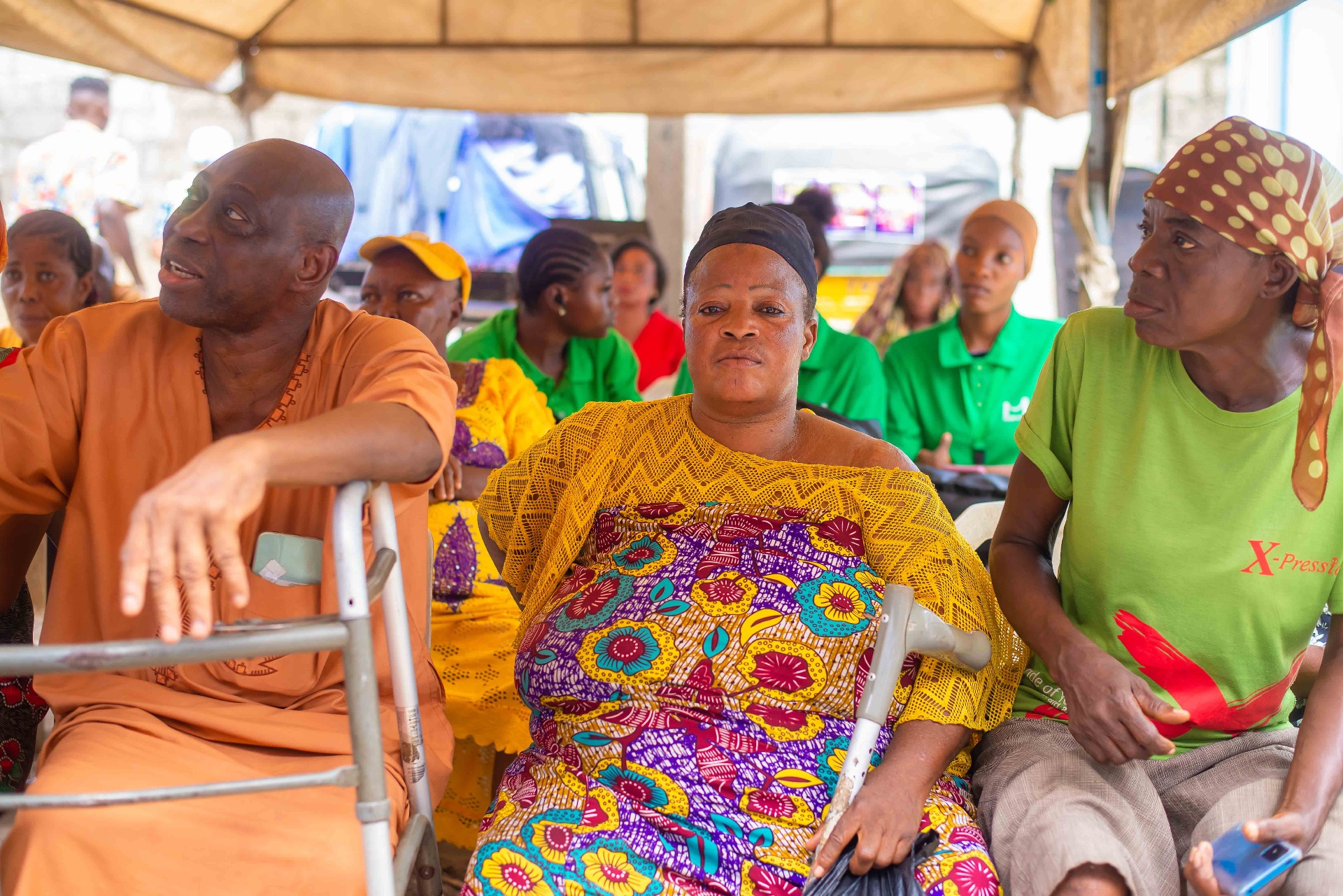 Community attendees seated under outreach tent